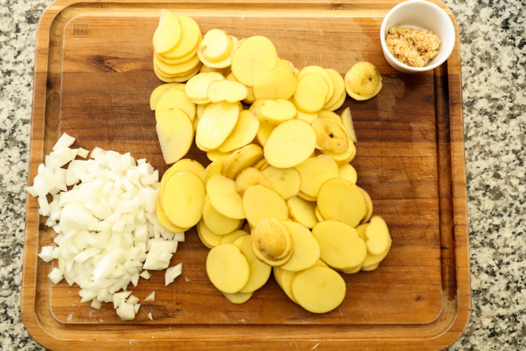 chopped onions, sliced potatoes, and minced garlic on cutting board
