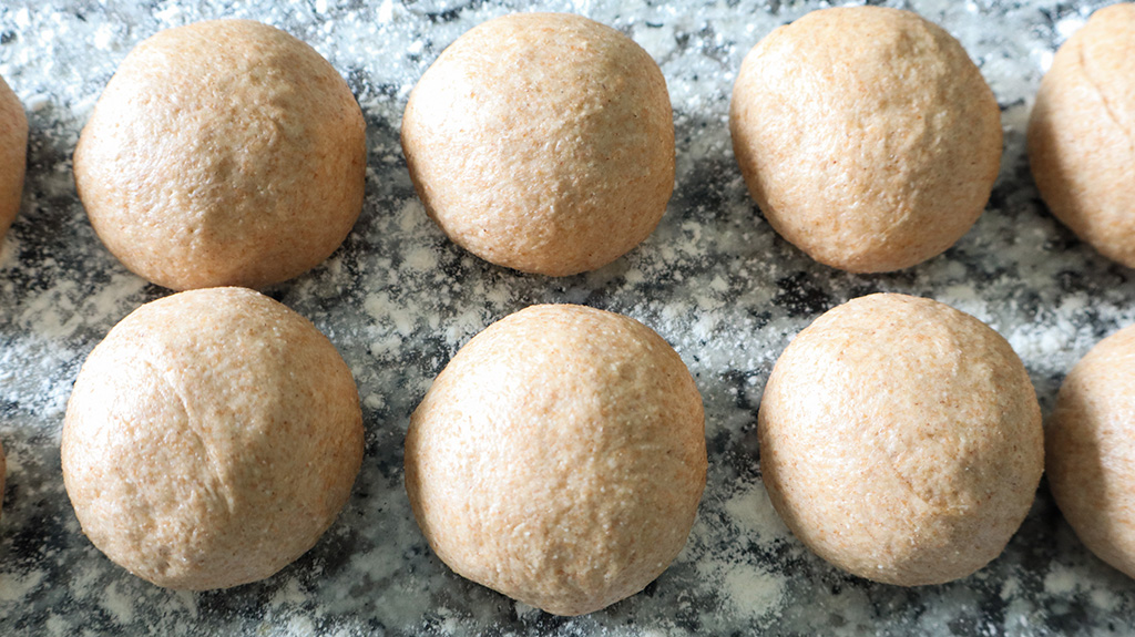 whole wheat tortilla dough balls on floured countertop
